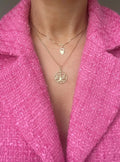 The heart padlock worn on a fine box chain, layered over the Libra pendant, against a pink jacket