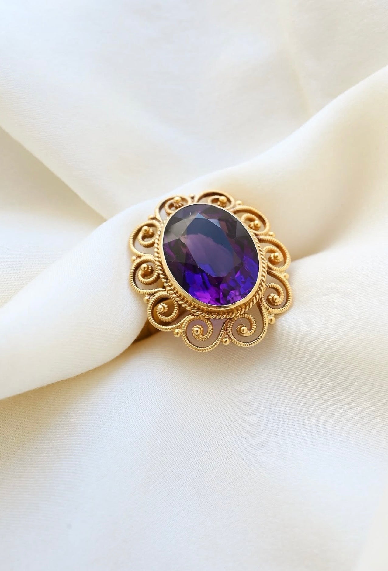 Antique amethyst filigree ring in 14K gold resting on ivory silk, the stone deep royal purple
