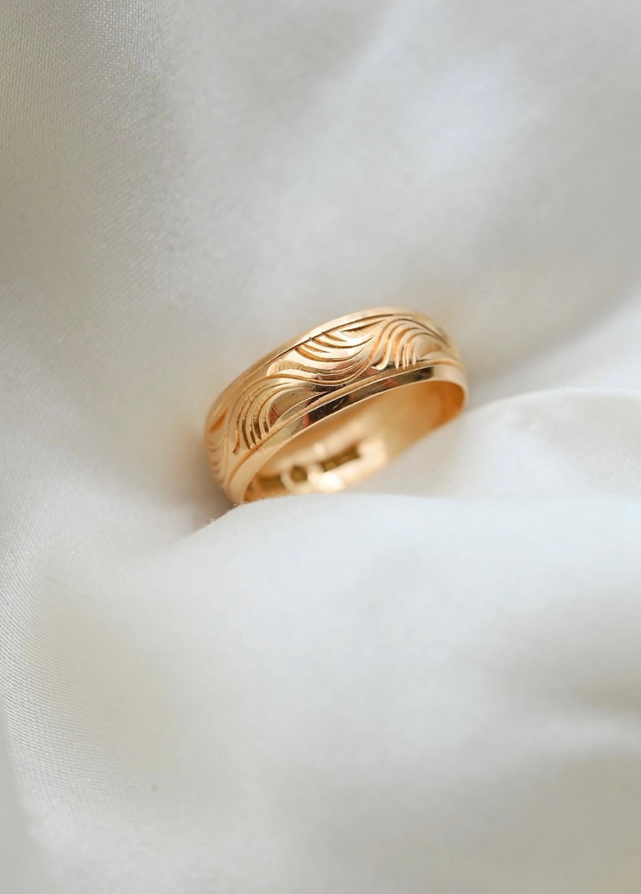 Wave engraved antique 18K gold wedding band from 1907 resting in ivory silk