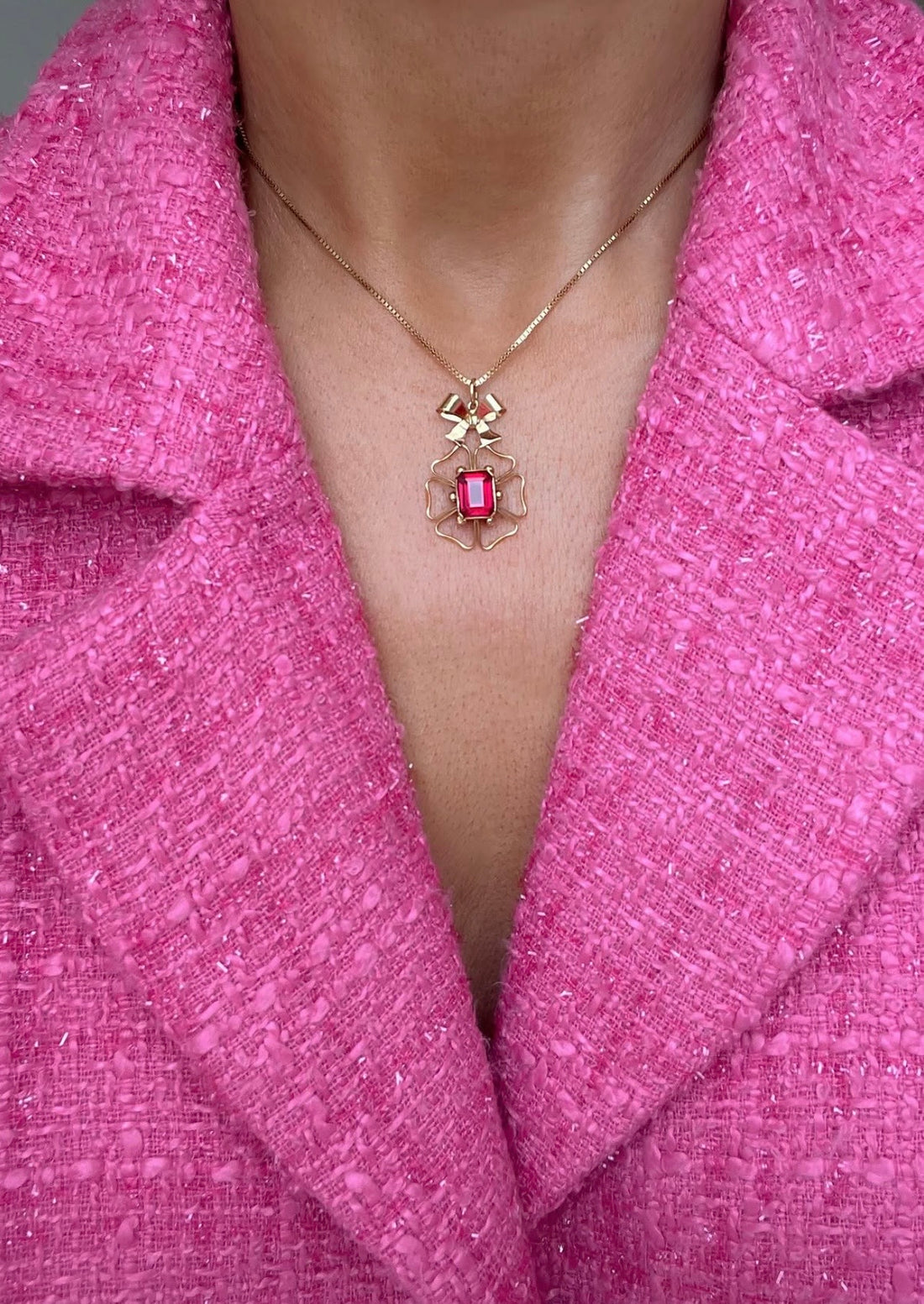 The cherry ruby bow pendant worn on a fine gold chain against a pink jacket