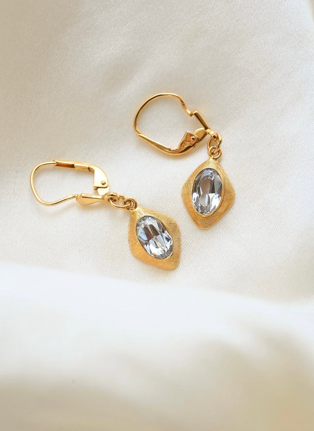 Vintage 18K gold drop earrings with icy pale spinels resting on ivory silk