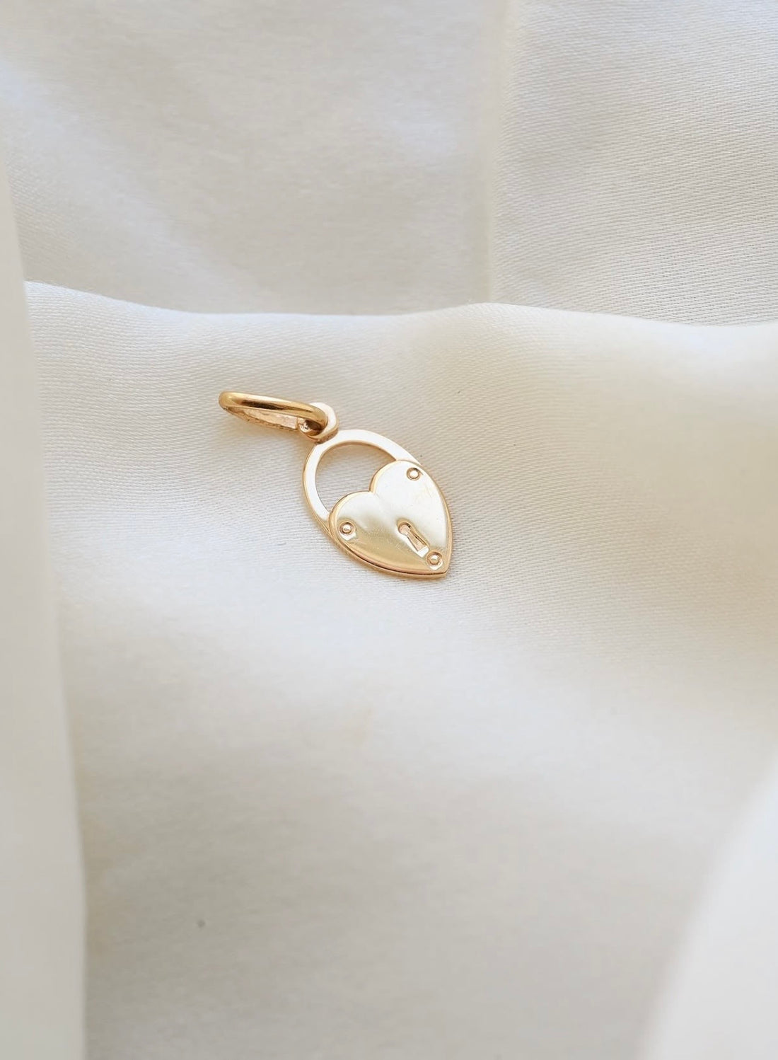 Tiny 18K gold heart padlock pendant made in Italy, resting on ivory silk