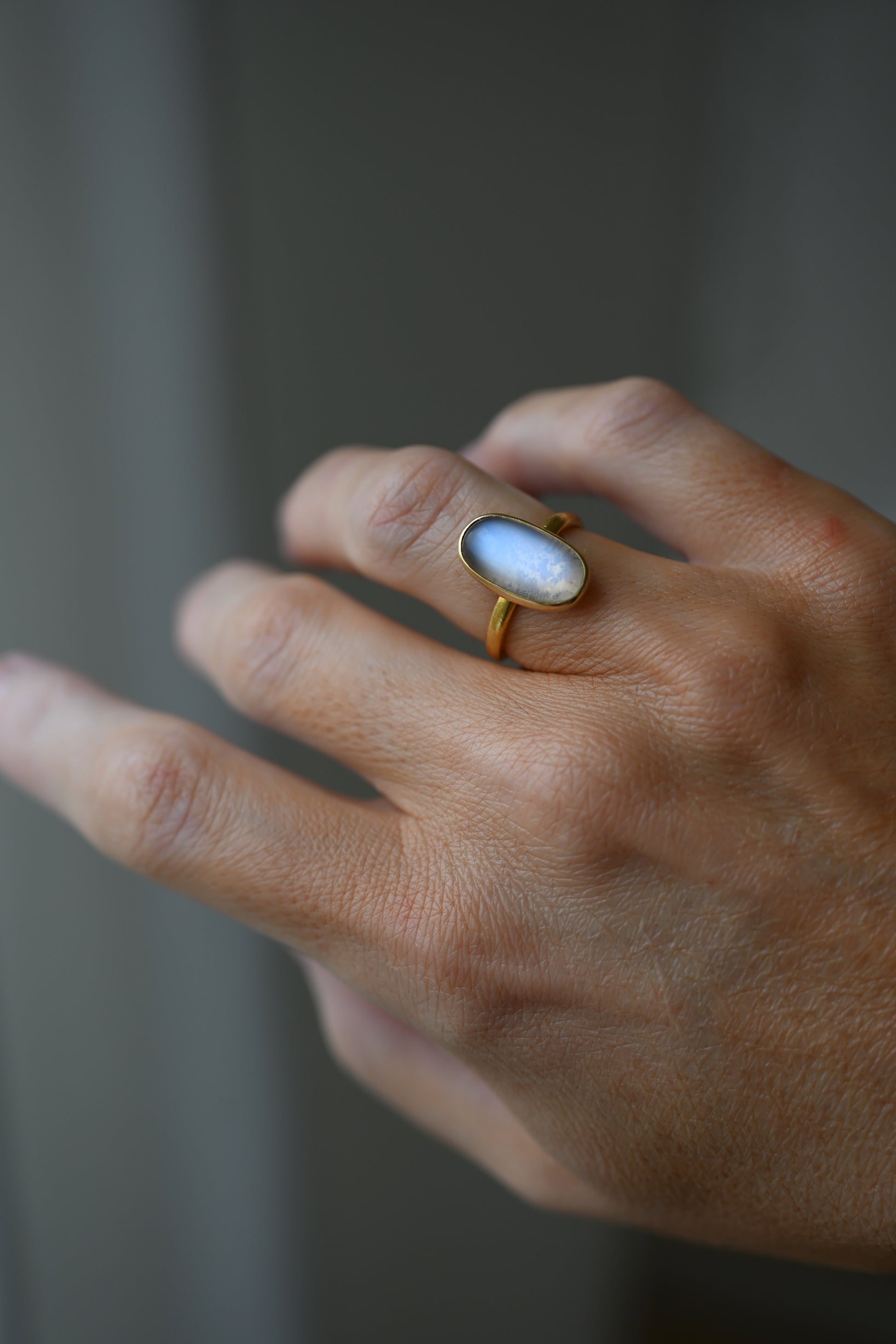 100 year old Swedish moonstone ring in 23K gold worn on the hand, the oval stone glowing blue