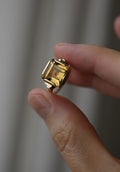 The ring held between two fingers, light passing through the golden citrine