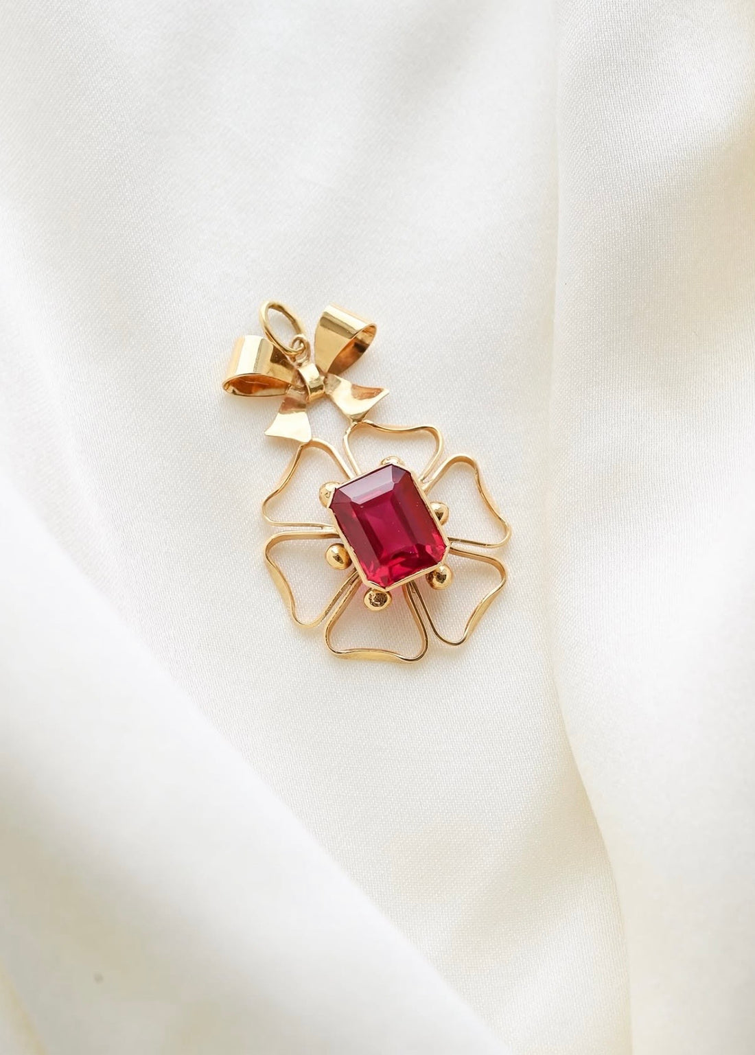 The cherry ruby bow pendant worn on a fine gold chain against a pink jacket