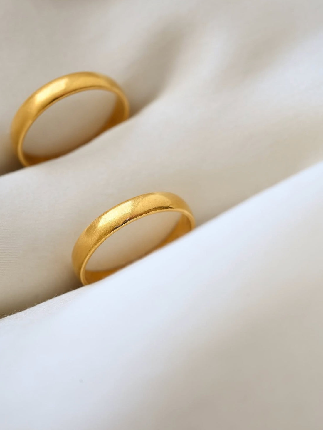 Two antique 23K gold wedding bands from 1896 and 1898 resting on ivory silk