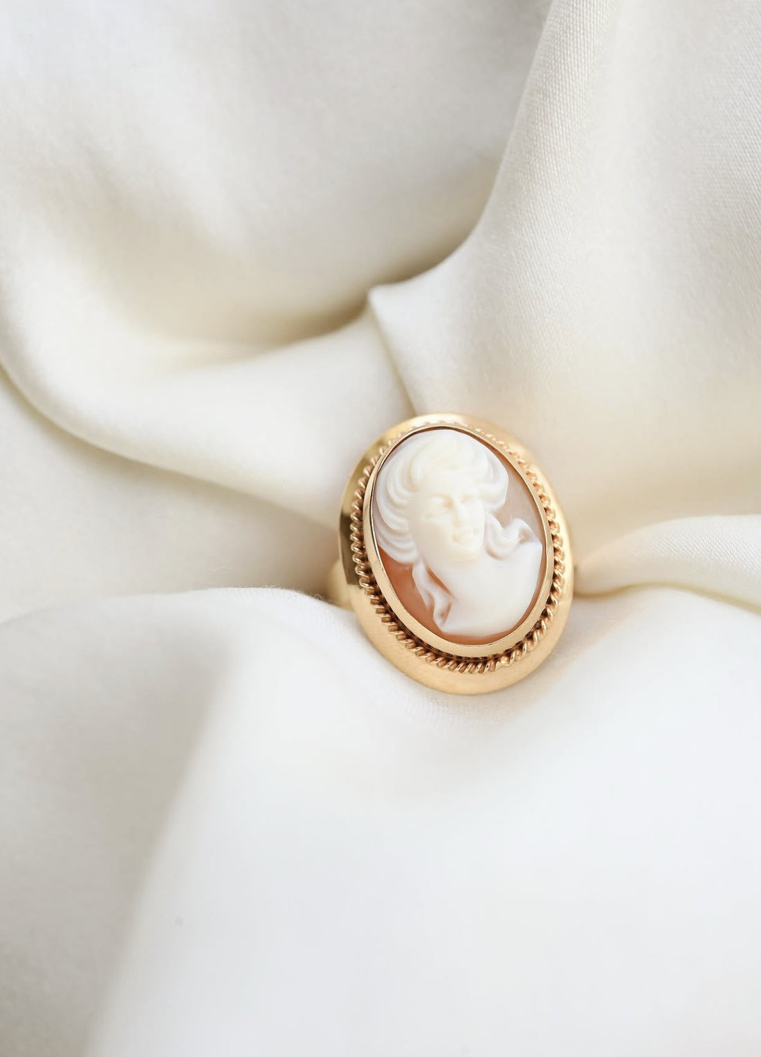 Vintage 18K gold cameo ring with twisted rope border resting on ivory silk