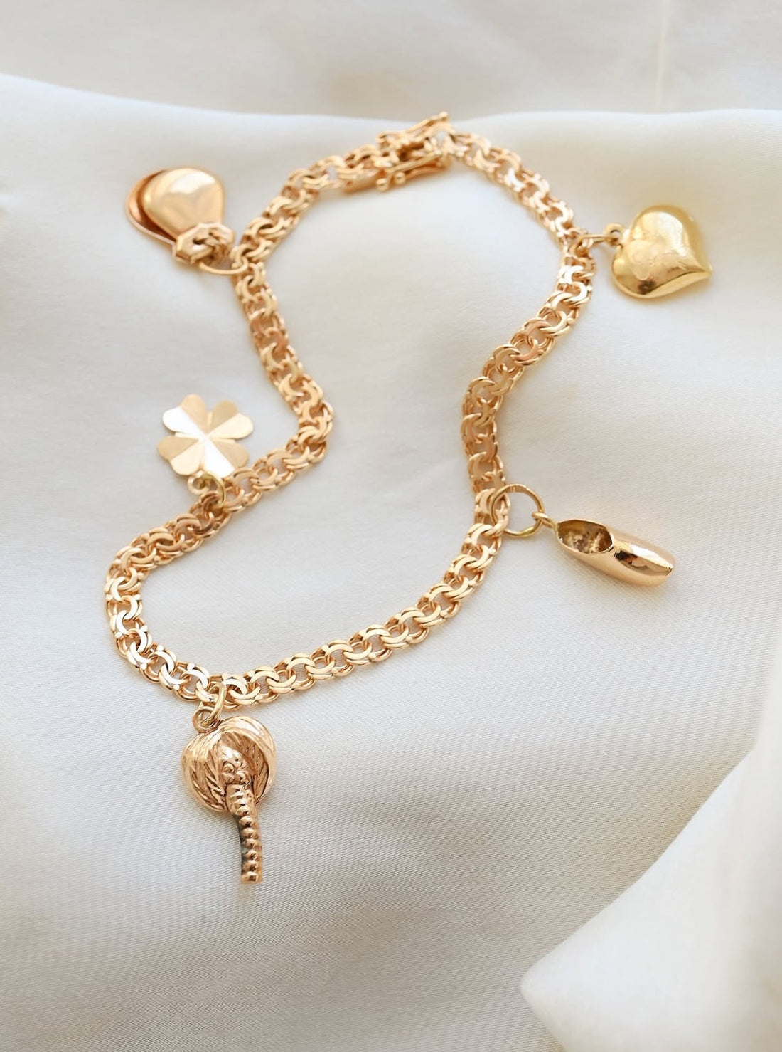 Vintage 18K gold charm bracelet with hearts, clover, shoe and palm tree charms on ivory silk