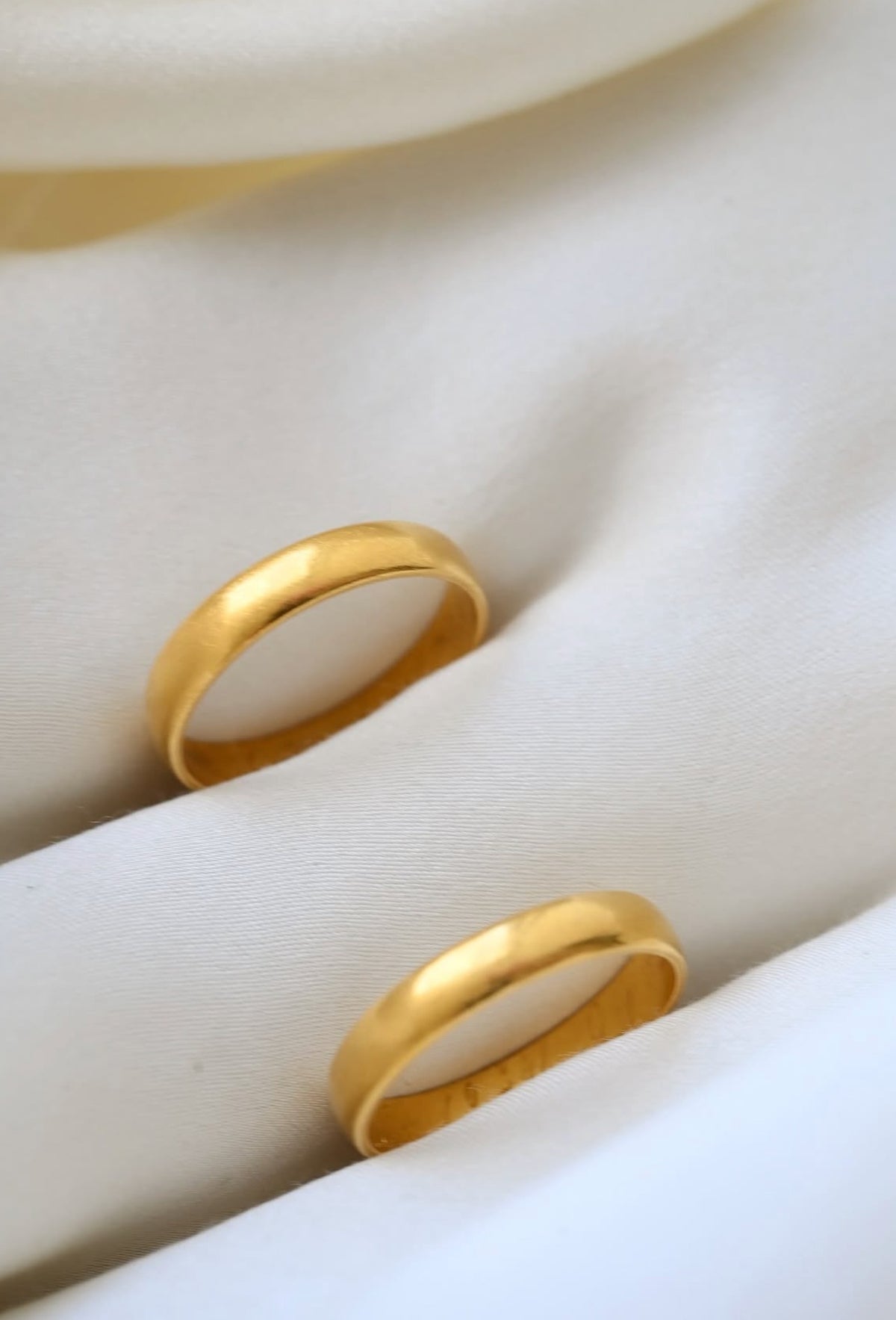 Two antique 23K gold wedding bands from 1896 and 1898 resting on ivory silk