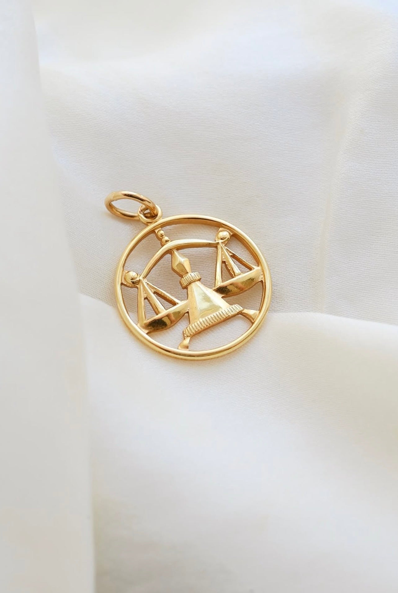 Vintage 18K gold Libra zodiac pendant with openwork scales, resting on ivory silk